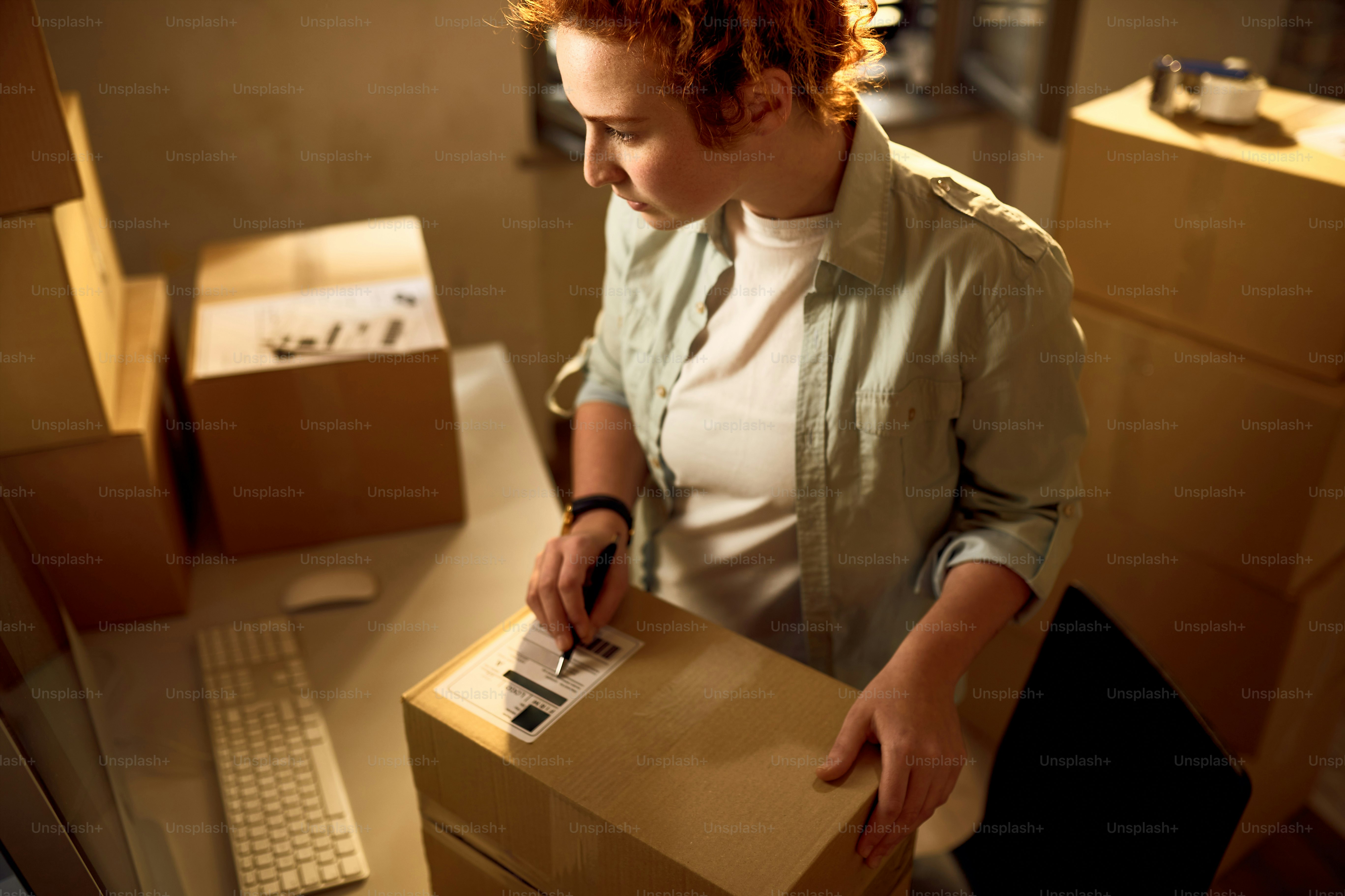 Junge Kurierin, die Computer benutzt und Daten für die Paketzustellung liest, während sie im Büro arbeitet.
