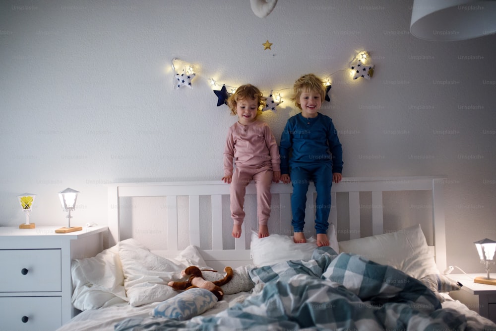 Two small laughing children playing on bed indoors at home, having fun.