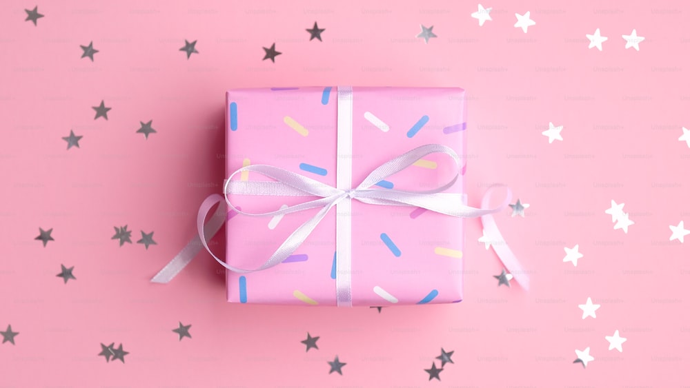 Bright pink gift box with silver sparkle confetti stars on pink background. Baby birthday surprise or valentine day present, love concept.