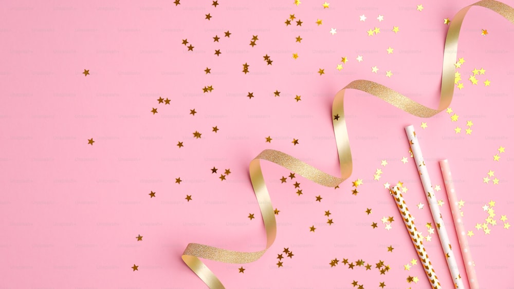 Goldenes Partydekor auf rosa Hintergrund. Flache Lay-Komposition mit Konfettisternen, Weihnachtsdekoration und Party-Streamer. Weihnachts-, Geburtstags- oder Hochzeitskonzept. Flache Lage, Draufsicht.