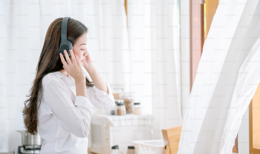 Young Asian woman listening music from headphone in teh kitchen