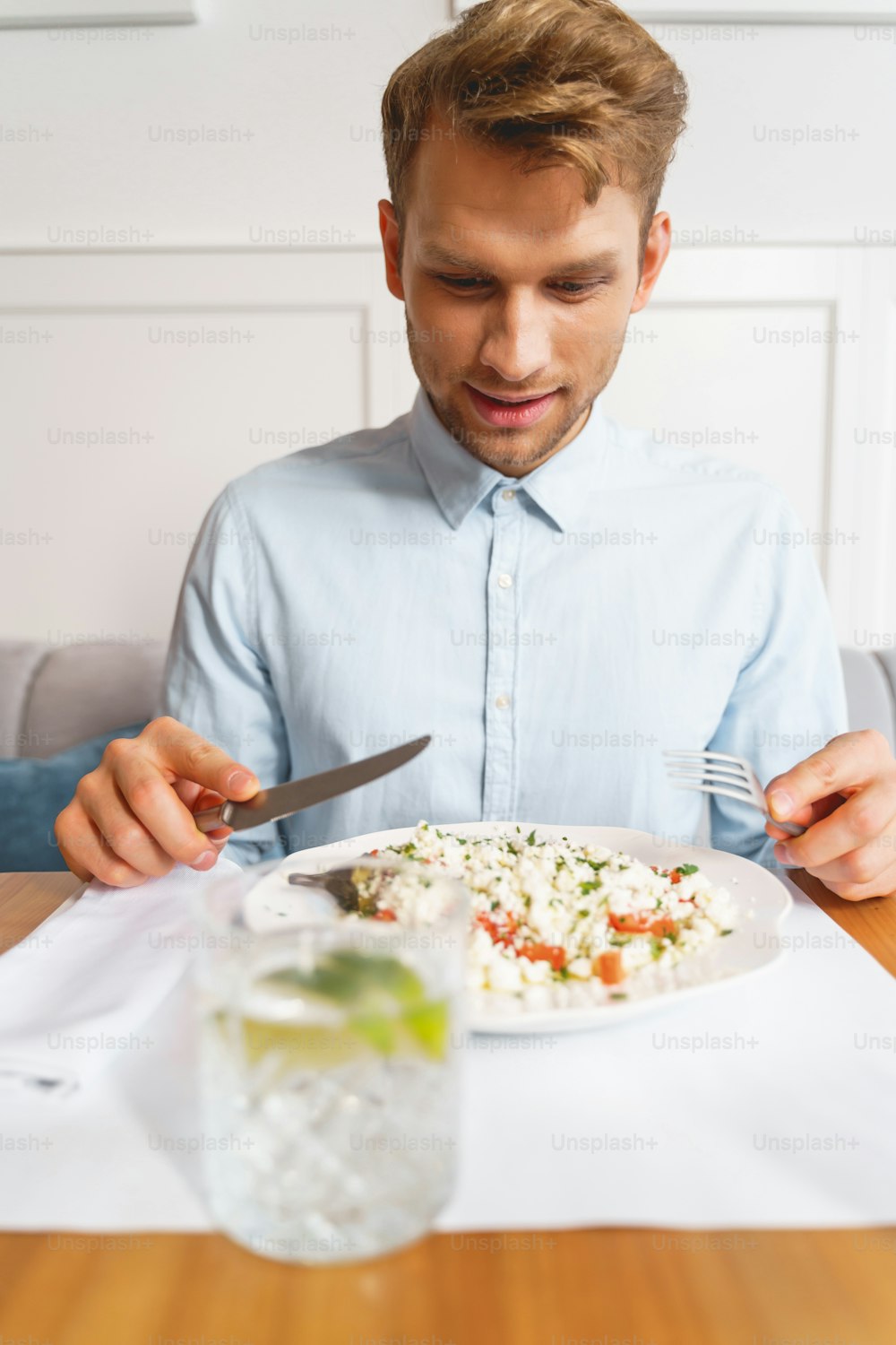 Gut aussehender Herr mit Gabel und Messer in der Hand sitzend am Tisch mit frischem Salat