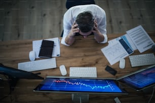 Top view of frustrated businessman with computer sitting and working at desk. Financial crisis concept.