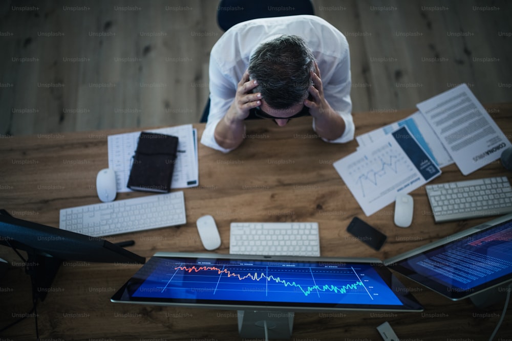 Vista superior de un hombre de negocios frustrado con la computadora sentada y trabajando en el escritorio. Concepto de crisis financiera.