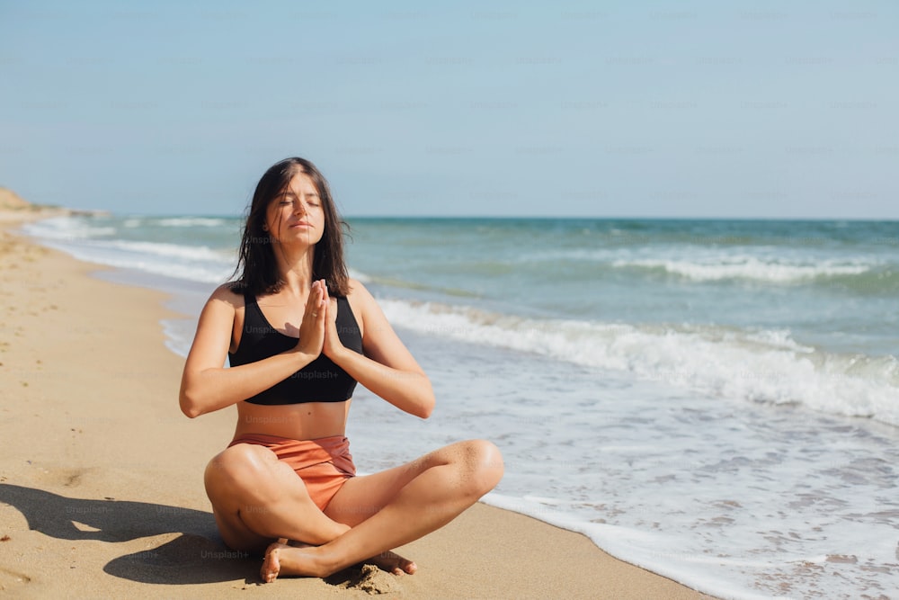 Concept de santé mentale et d’autosoins. Jeune belle femme pratiquant le yoga sur la plage, assise sur le sable et méditant. Fille heureuse se relaxant au bord de la mer pendant les vacances d’été