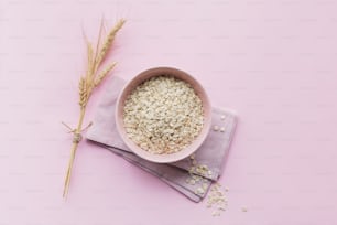 Bowl of dry oatmeal with ears of wheat on light background with copy space for text. Cooking oats porridge concept. Flat lay