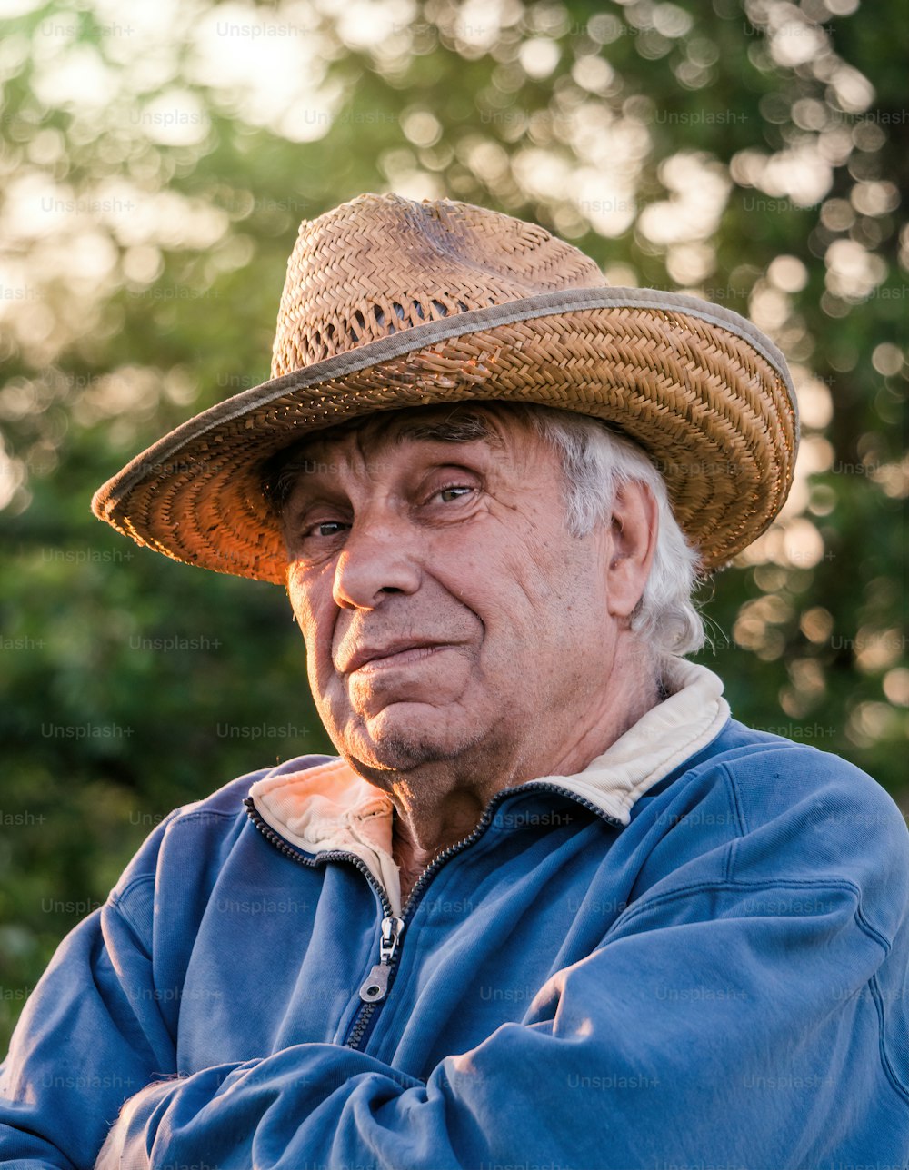 Portrait of an elderly gray-haired man in a straw hat on a background of a sunny spring garden and sunset sky. Peaceful retired village life