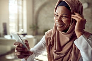 Felice donna d'affari islamica nera che usa il telefono cellulare e i messaggi di testo mentre lavora in ufficio.