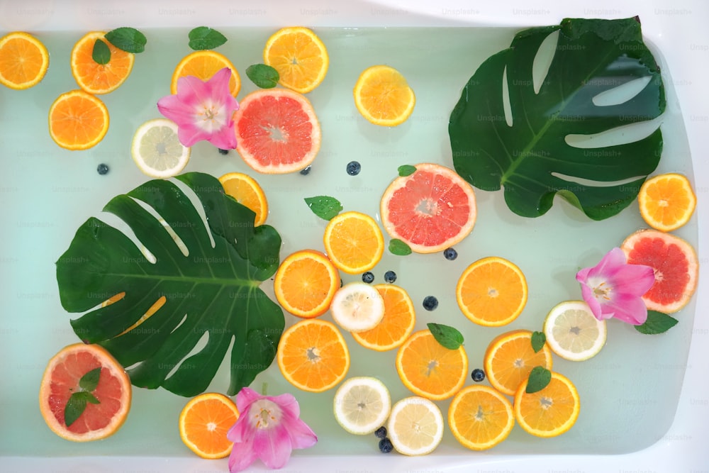 Bain relaxant avec des pamplemousses, du citron, des tranches d’oranges et des fleurs. Soin de beauté. Concept de bien-être