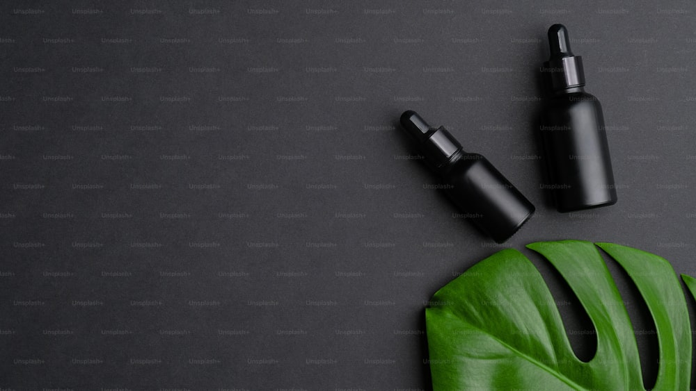 Luxury cosmetic bottles and tropical monstera leaf on black background. Premium hair oil bottles mockup. Natural organic beauty product for hair care and treatment concept