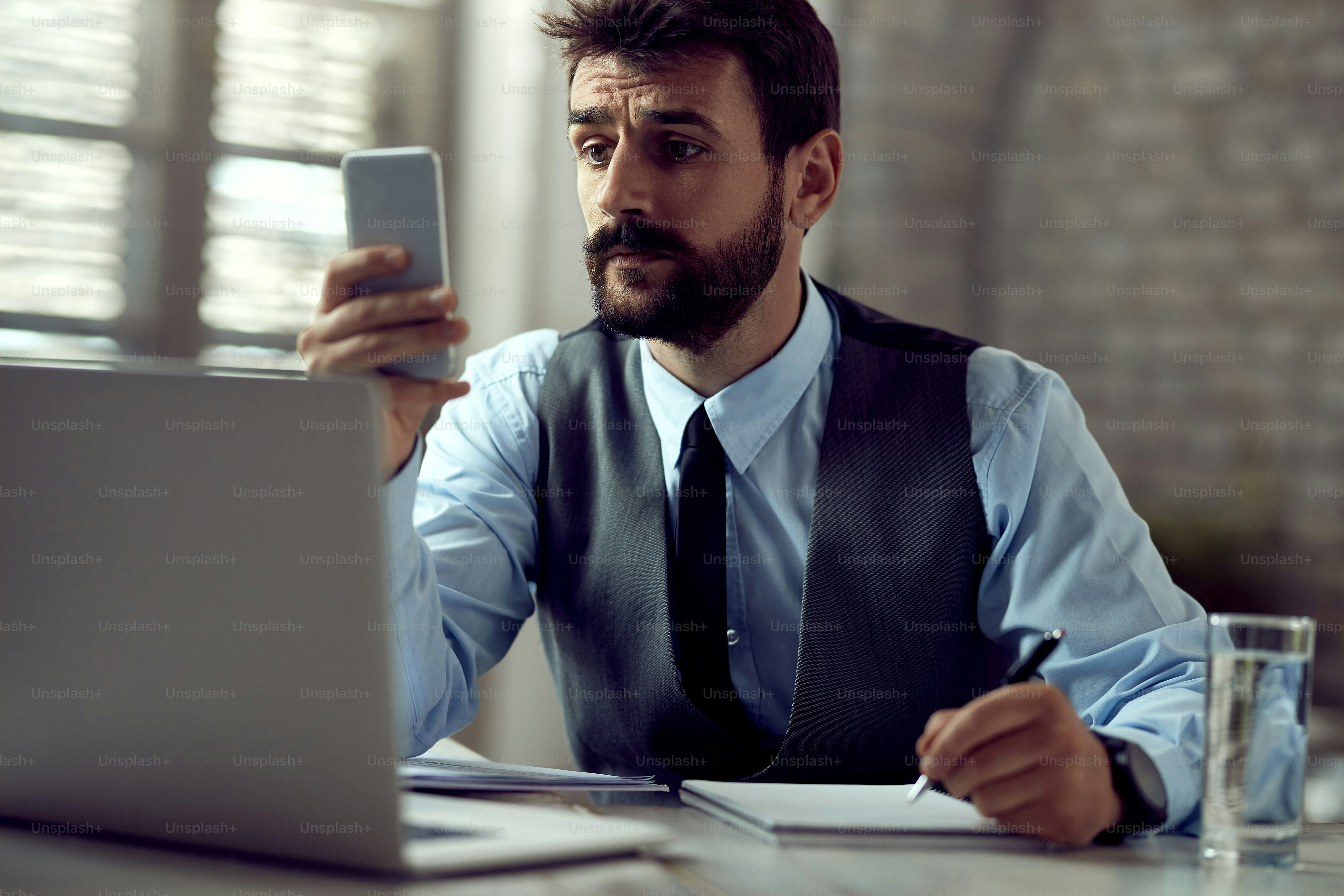 Male entrepreneur using mobile phone and text messaging while taking notes in the office
