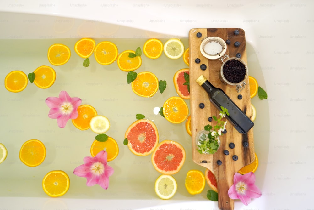 Bagno rilassante con fette di pompelmo, limone e arance. Prodotti per trattamenti di bellezza su tavola rustica in legno. Concetto di benessere