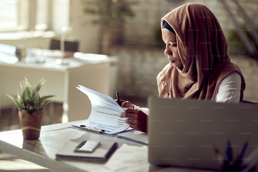 Black Muslim female entrepreneur analyzing business reports while working in the office.