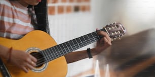 어쿠스틱 기타에 대한 기술을 연습하는 젊은 아시아 여성의 자른 이미지, 거실 흰 벽을 배경으로 앉아 있다. 어쿠스틱 기타 컨셉을 연주하는 여성.