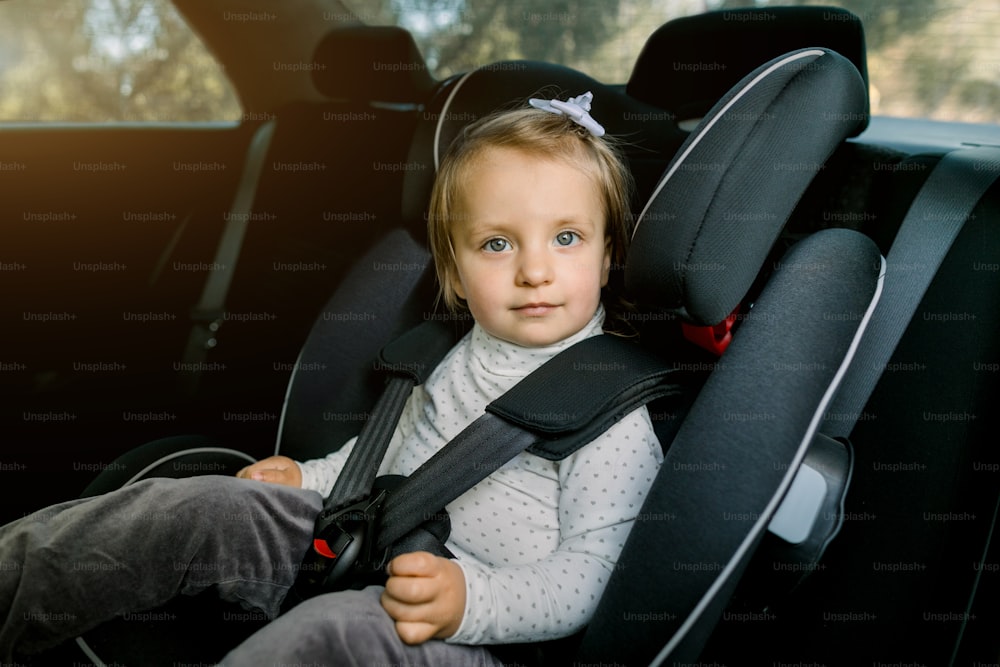Transport, safety, childhood road trip and people concept. Happy Caucasian cute little baby girl sitting in baby car seat. Child in auto baby seat in car. Adorable little girl in the car