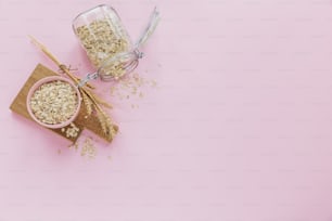 Bowl of dry oatmeal with ears of wheat on light background with copy space for text. Cooking oats porridge concept. Flat lay