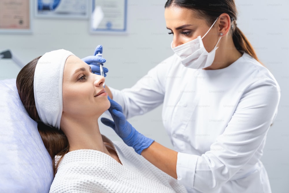 Dermatólogo profesional con guantes de látex estériles desechables que minimizan los pliegues nasolabiales en la cara de una mujer joven