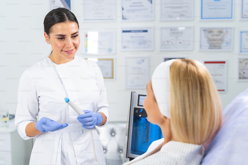 Smiling beautiful young female dermatologist holding a microcurrent facial device in front of her patient