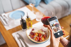 Close up of female hands holding mobile phone and photographing fresh salad and alcoholic drink in cafe