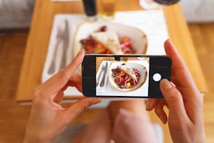 Close up of female hands holding cellphone and photographing fresh salad in cafe