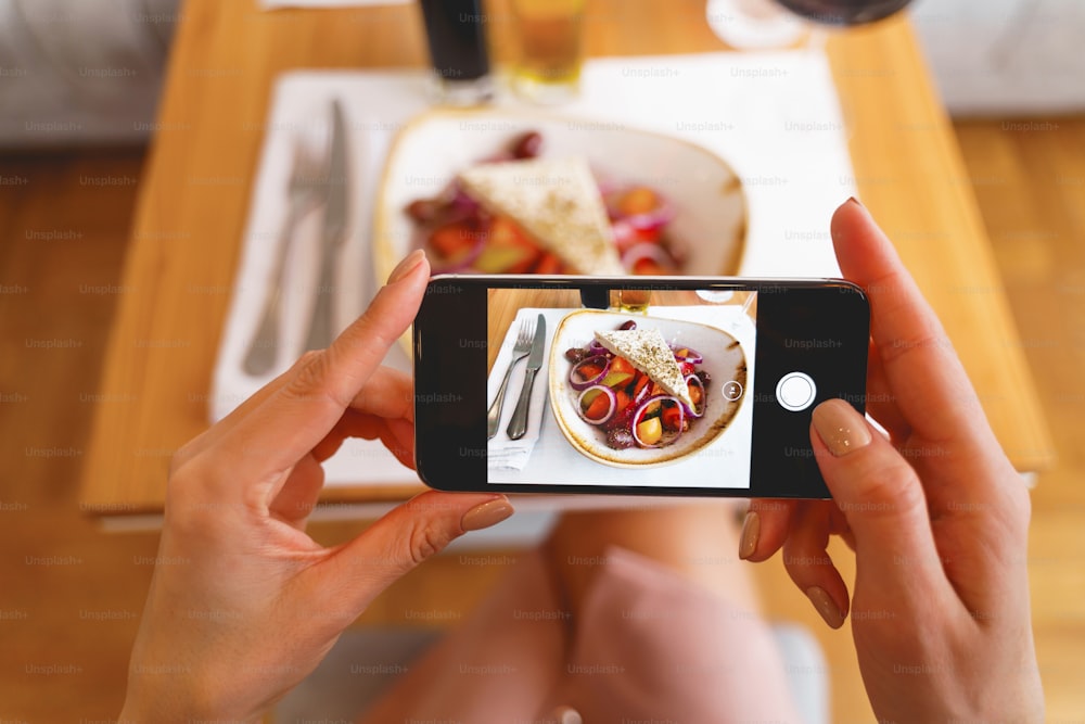 携帯電話を持ち、カフェで新鮮なサラダを撮影する女性の手の接写