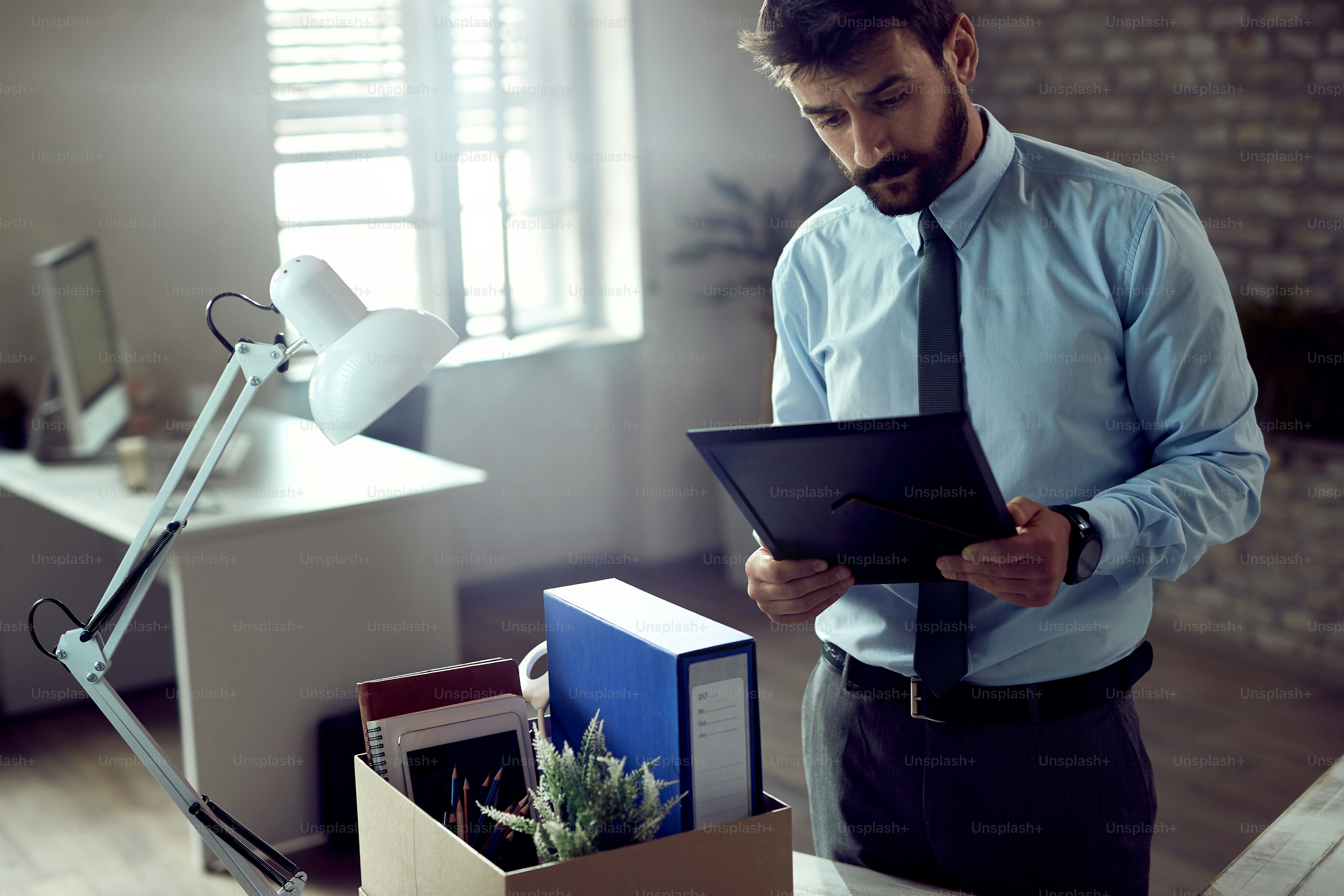 Young entrepreneur feeling sad while looking at picture in photo frame after being fired at work