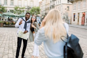 Excited cheerful mix raced couple, African man and Caucasian girl, enjoying walking outdoors, in the center of ancient European city, while their pretty female friend is making photo of them.
