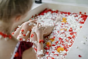 Natural skin care concept. Selective focus on woman legs in bathtub with tropical flowers. Young adult girl lying in bath and enjoying spa procedure