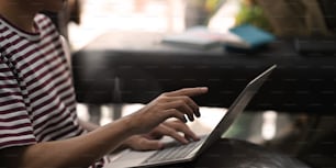 Cropped shot creative man typing on computer laptop that putting on his lap while sitting at the leather couch over comfortable.