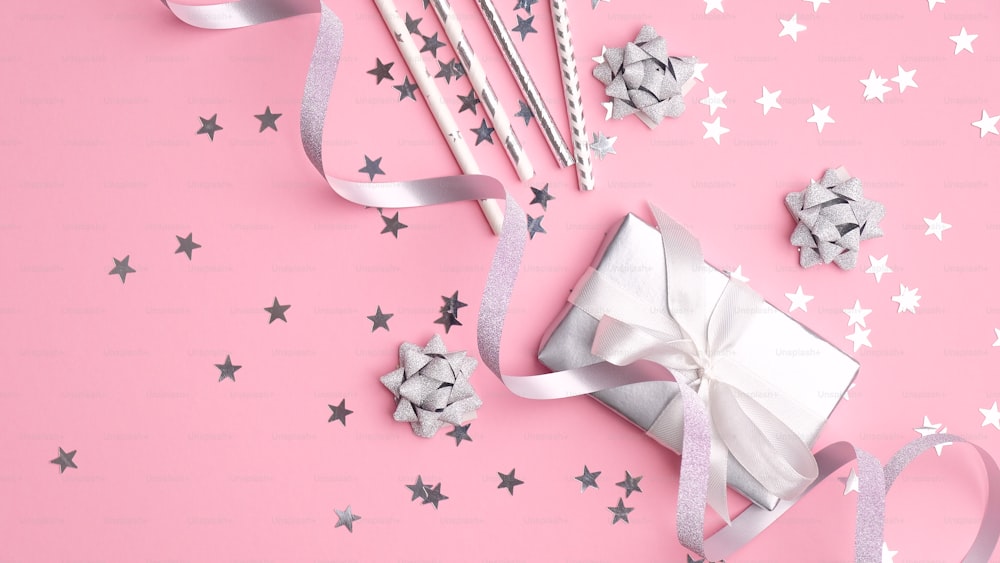 Silver metallic gift box and party decorations with confetti stars on pink background. Festive flat lay composition for girls birthday, Christmas party or wedding