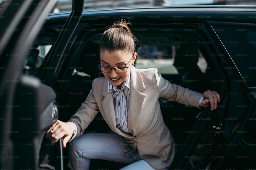 Giovane donna d'affari di bell'aspetto seduta sul sedile posteriore in un'auto di lusso. Usando il suo smartphone, sorridendo e guardando fuori. Il trasporto nel concetto di business aziendale.