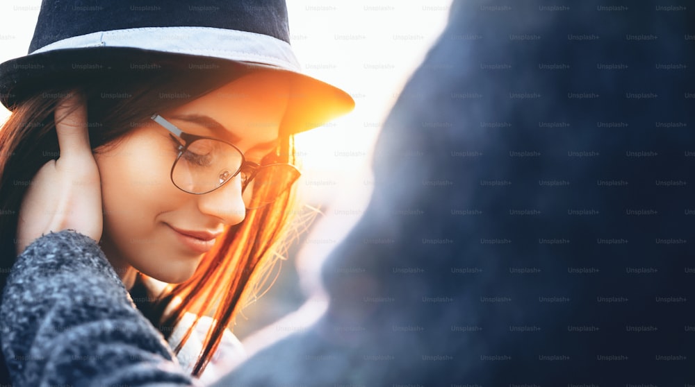 Lovely women with hat and eyeglasses looking down is touched by her lover posing in a sunny evening