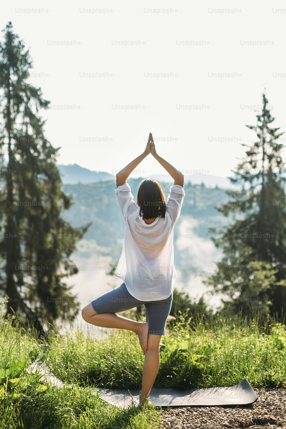 Young woman practicing yoga among grass on background of morning mountains in sunny light. Meditation. Calm tranquil moment, connection with nature. Copy space