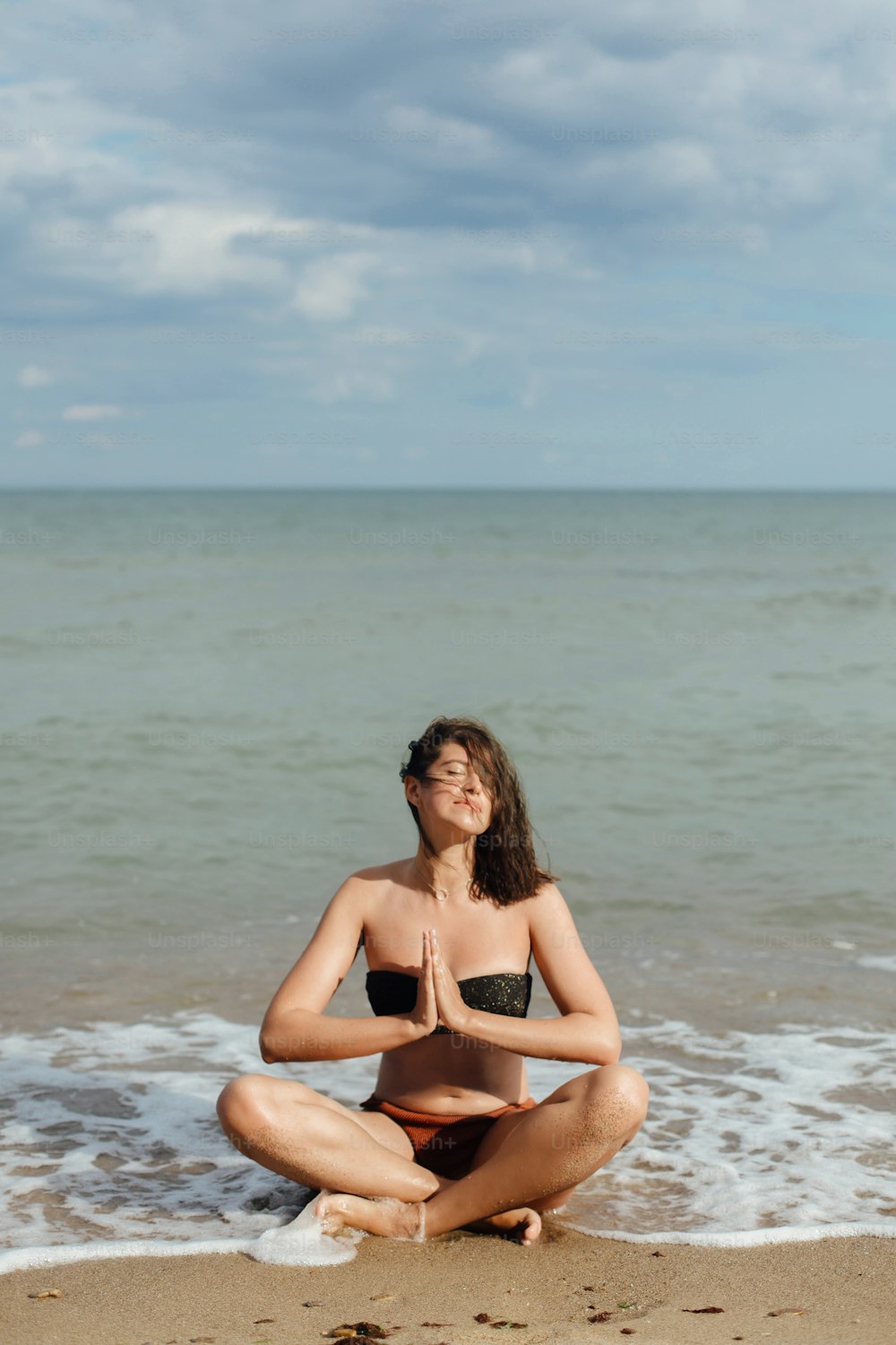 Concept de santé mentale et d’autosoins. Jeune belle femme pratiquant le yoga sur la plage, assise sur le sable et méditant. Fille heureuse se relaxant au bord de la mer pendant les vacances d’été