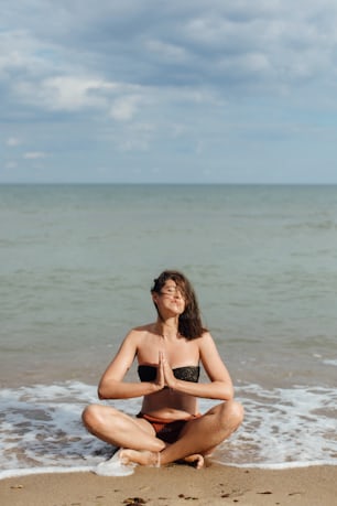 Mental health and self care concept. Young beautiful woman practicing yoga on the beach, sitting on sand and meditaning. Happy girl relaxing on seashore on summer vacation