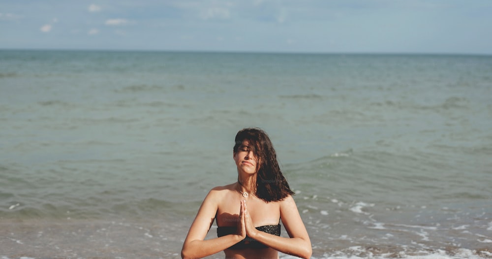 Jeune belle femme pratiquant le yoga sur la plage, assise sur le sable et méditant. Concept de santé mentale et d’autosoins. Fille heureuse se relaxant au bord de la mer pendant les vacances d’été