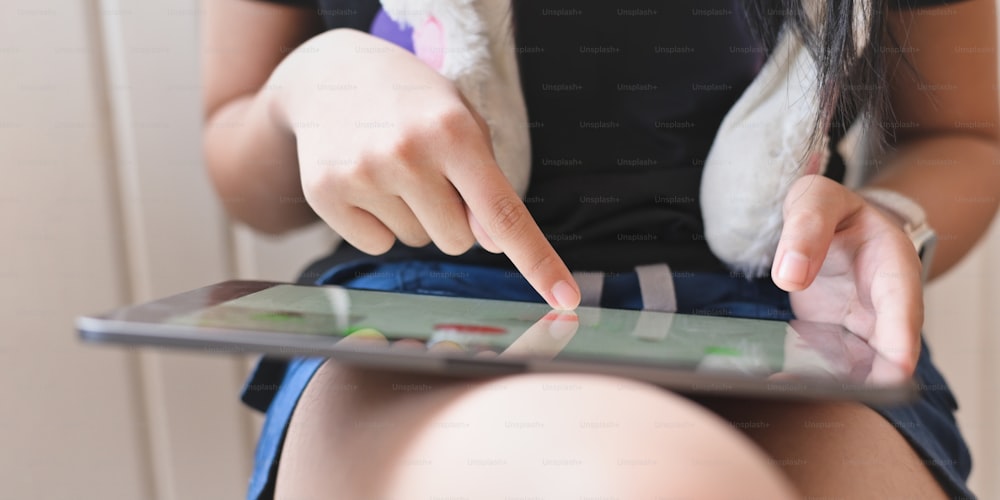 편안한 거실에 앉아 무릎을 꿇고 컴퓨터 태블릿을 사용하는 아름다운 소녀의 자른 이미지.