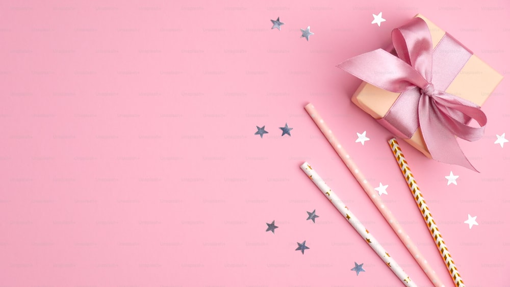 ピンクのテーブルトップビューに紙吹雪の星が描かれたギフトボックスとストロー。女の子の誕生日、結婚式、クリスマスパーティーのコンセプト。