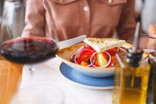 Close up of lady holding fork and knife while sitting at the table with glass of wine and fresh salad with vegetables