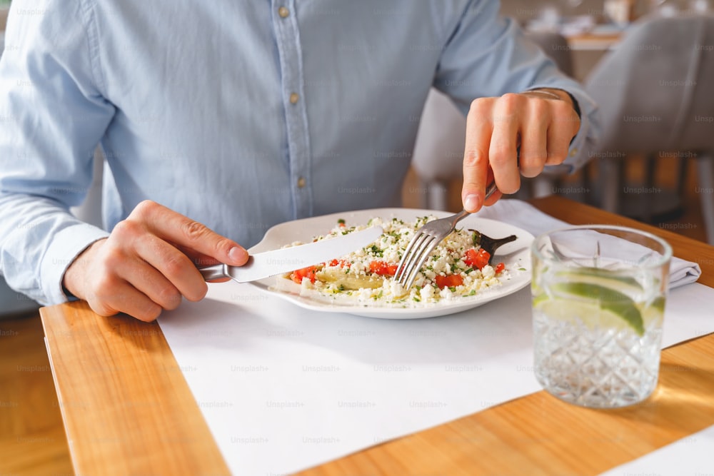 Close up of gentleman holding fork and knife while sitting at the table with healthy food and glass of water