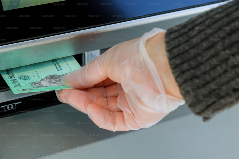 Close up da mão entrando no cheque de estímulo do depósito para a transfer�ência da máquina ATM