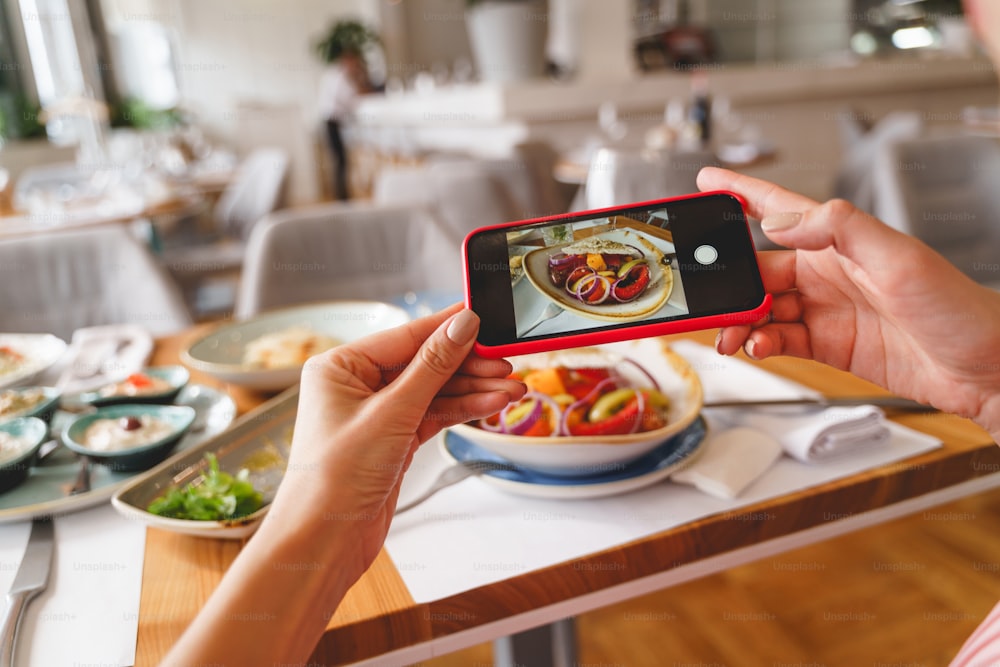 スマートフォンを持ち、カフェで新鮮なサラダを撮影する女性の手の接写