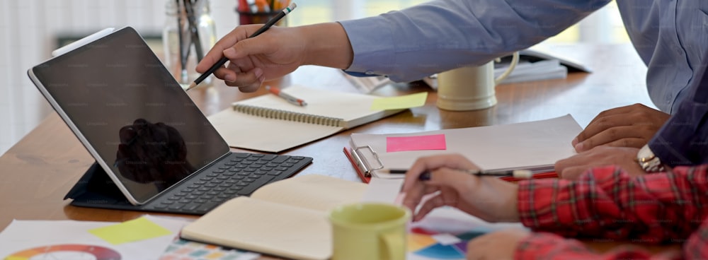 Vista lateral de empresários que prestam consultoria em seu projeto com tablet digital, notebooks e papelaria em mesa de trabalho