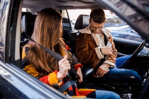 Hombre y mujer jóvenes en un automóvil abrochándose los cinturones de seguridad antes de conducir