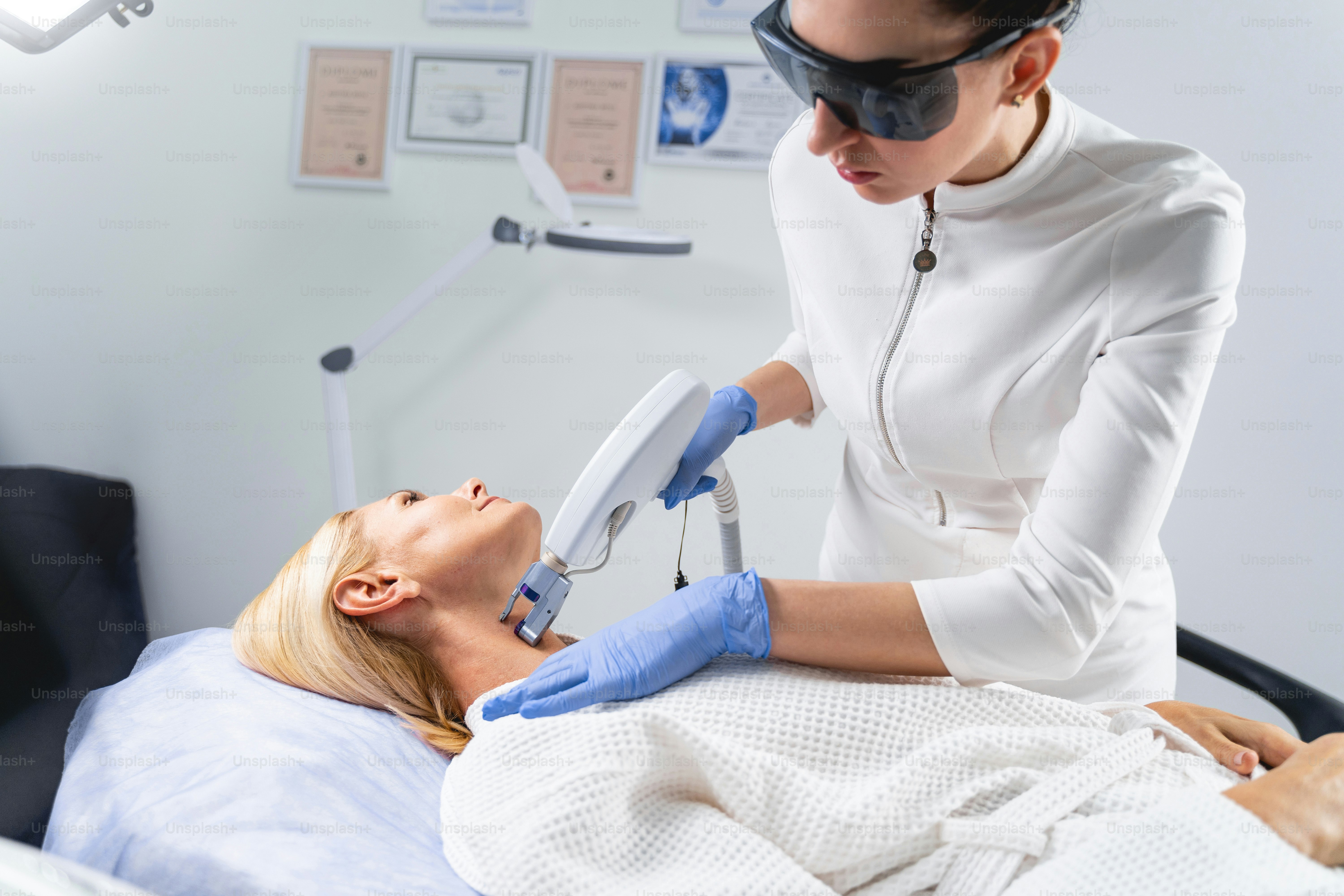 Focused young female doctor in protective goggles reducing fine lines on a mature patient neck