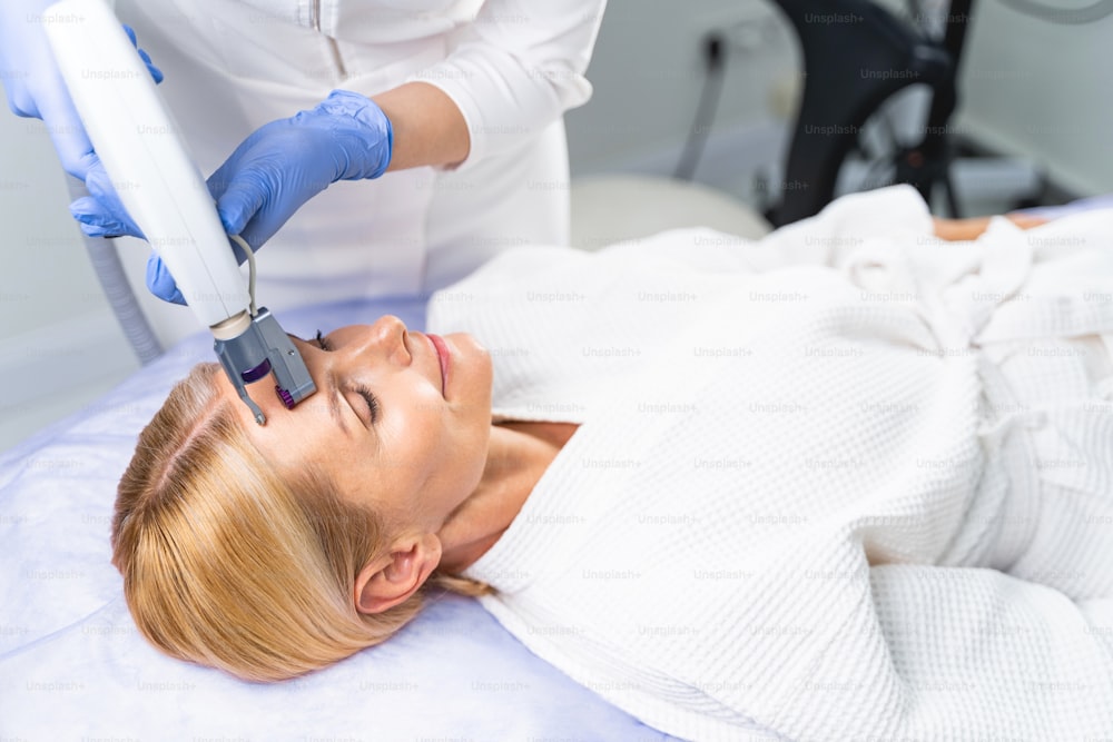 Cosmetologista profissional suavizando rugas na testa da mulher com um dispositivo especial