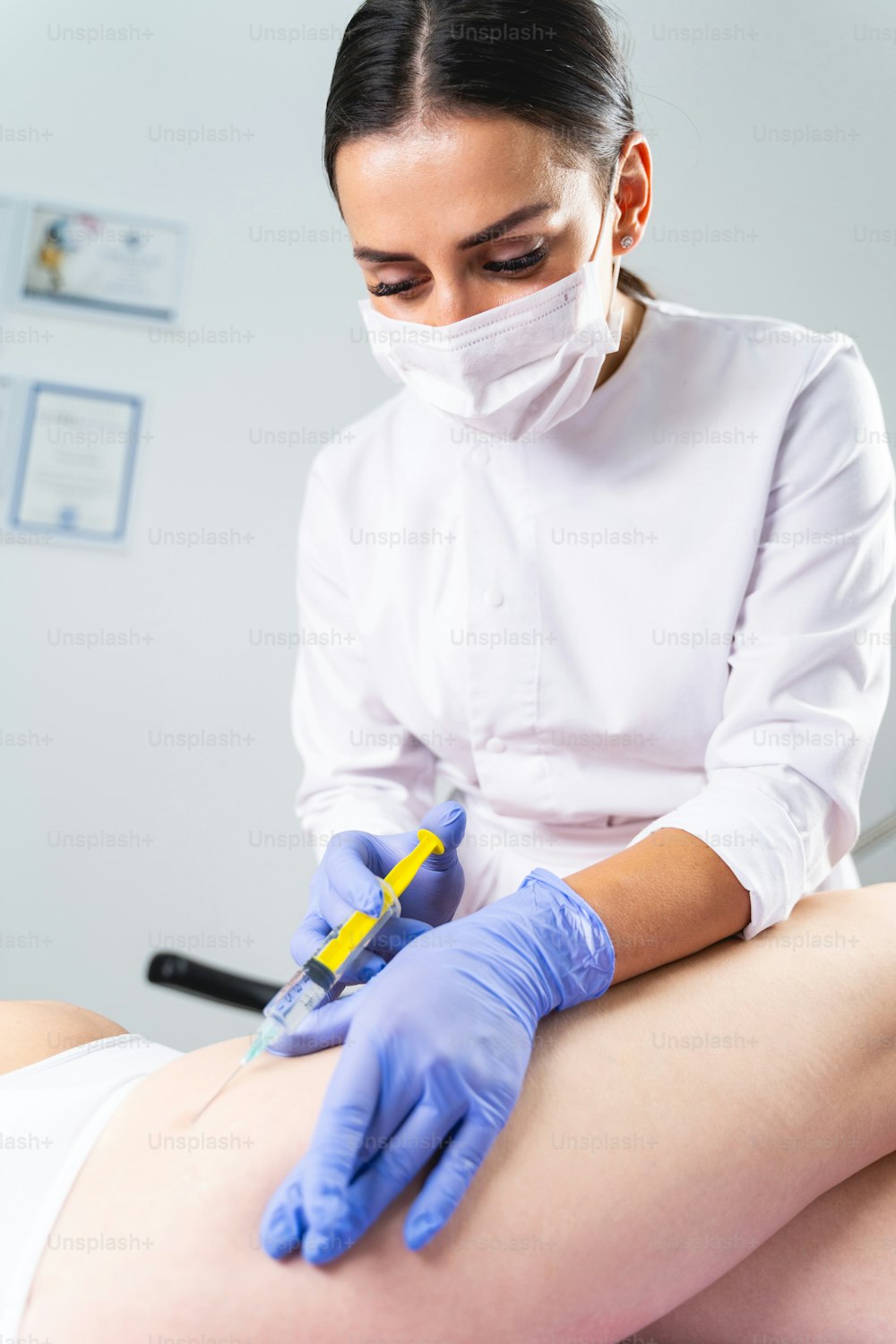 フェイスマスクを着けた黒髪の若い女性皮膚科医が妊娠線のメソセラピーを行う