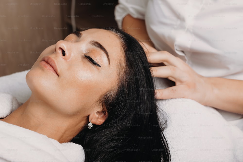 Close up retrato de uma mulher caucasiana com cabelo preto deitado no sofá durante um procedimento de massagem na cabeça