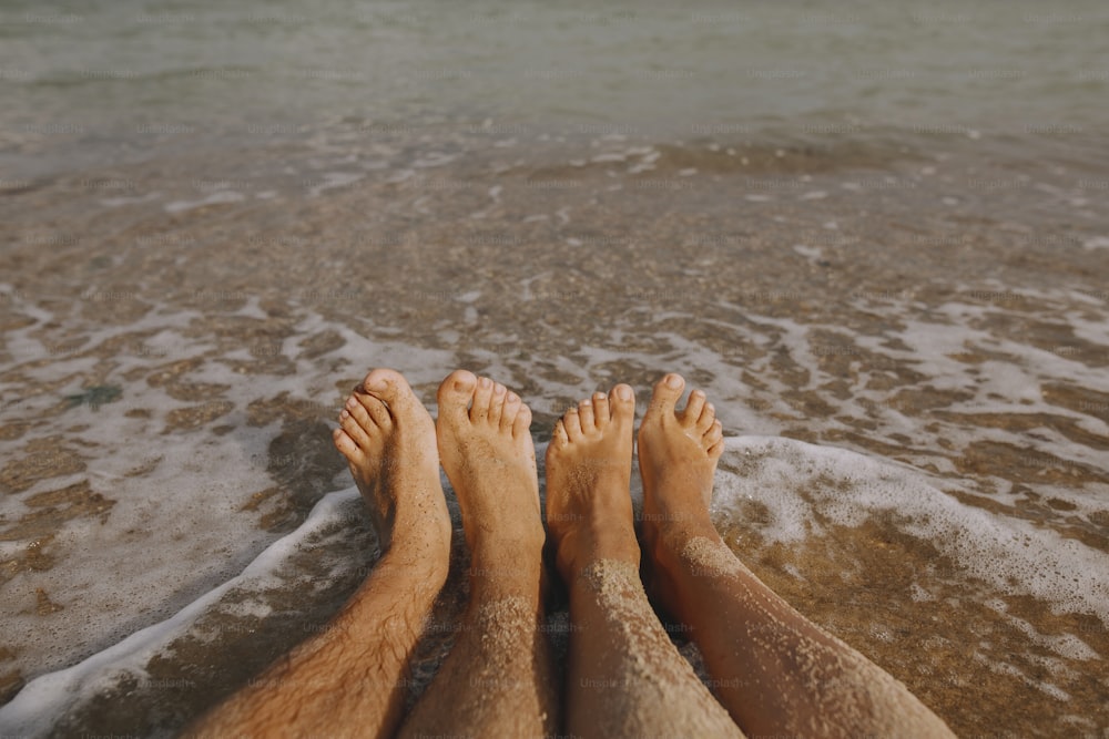 波のある日当たりの良いビーチで砂浜のカップルの濡れた足のクローズアップ。砂浜で一緒にリラックスする愛のカップル。家族での夏休みや新婚旅行の大切なひととき。本物のイメージ