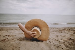 Sommerurlaub und Reisen. Mädchen mit Hut liegt am Strand. Modische junge Frau mit Strohhut, die sich am Sandstrand in der Nähe des Meeres entspannt. Achtsamkeit und unbeschwertes kreatives Image
